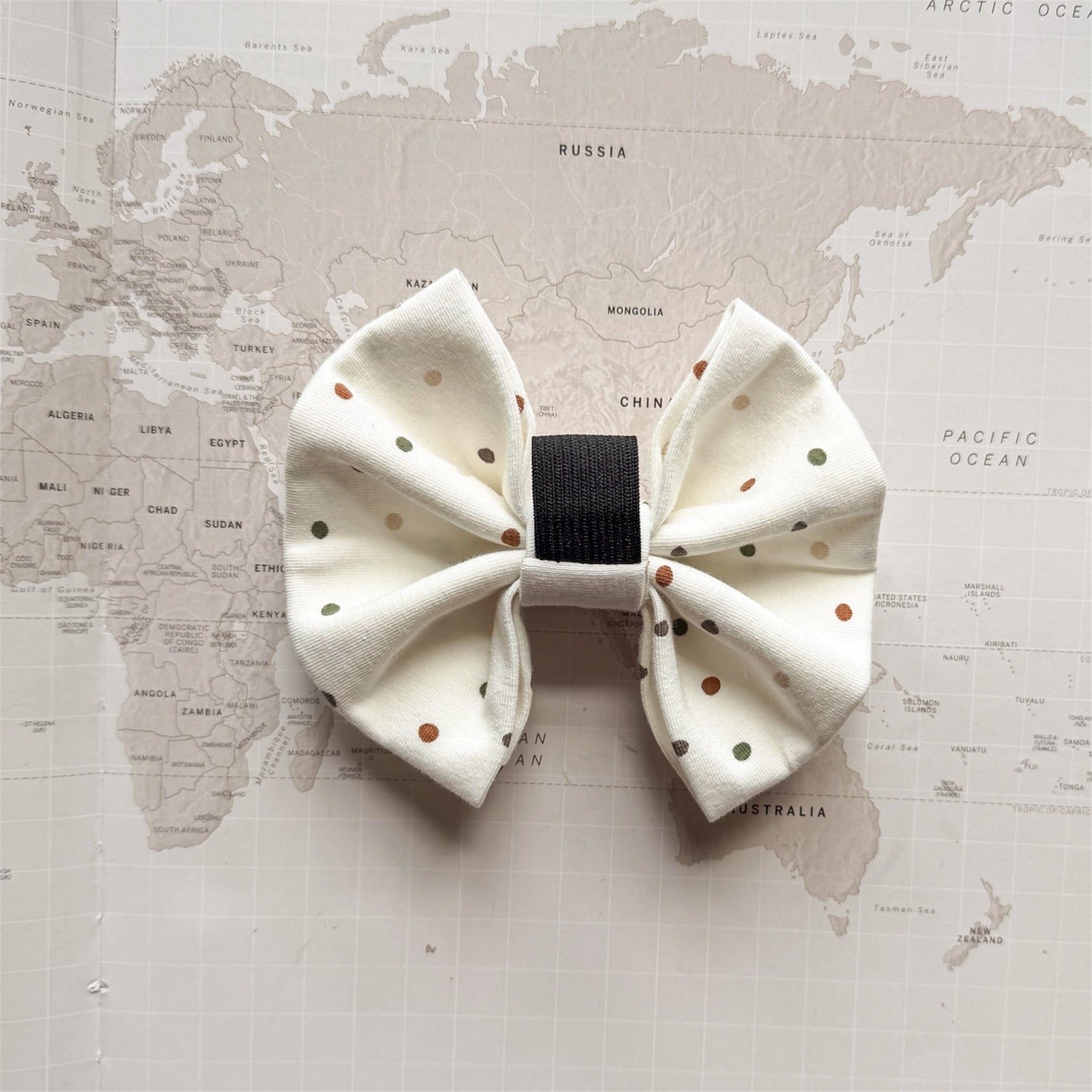 Back of the white dog bow with brown and green polka dots and elastic loop on a world map background.