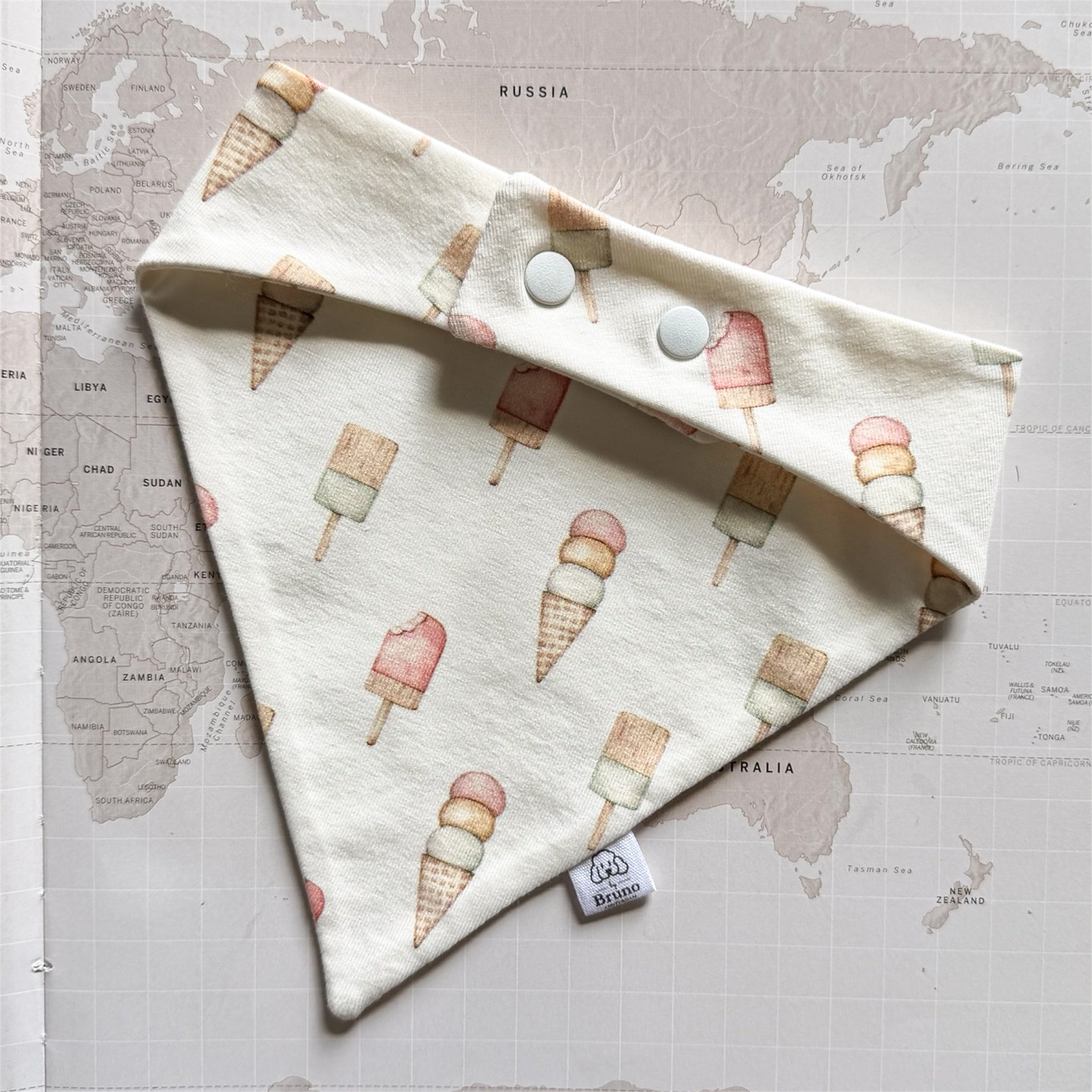Back side of the handmade beige dog bandanna with pastel ice creams on a world map background.