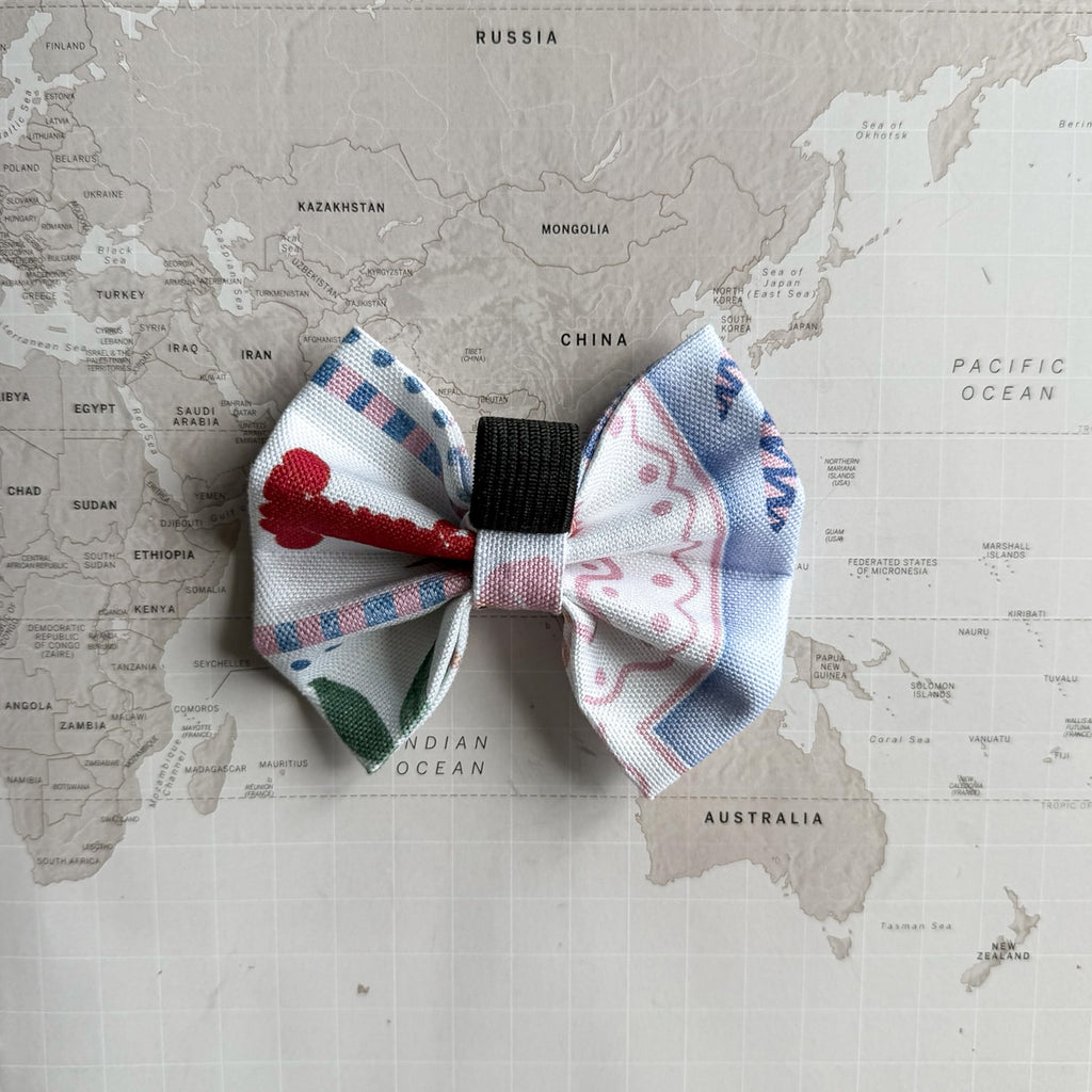 Back side of the handmade dog bow with pastel palm tree and the elastic loop on a world map background. 
