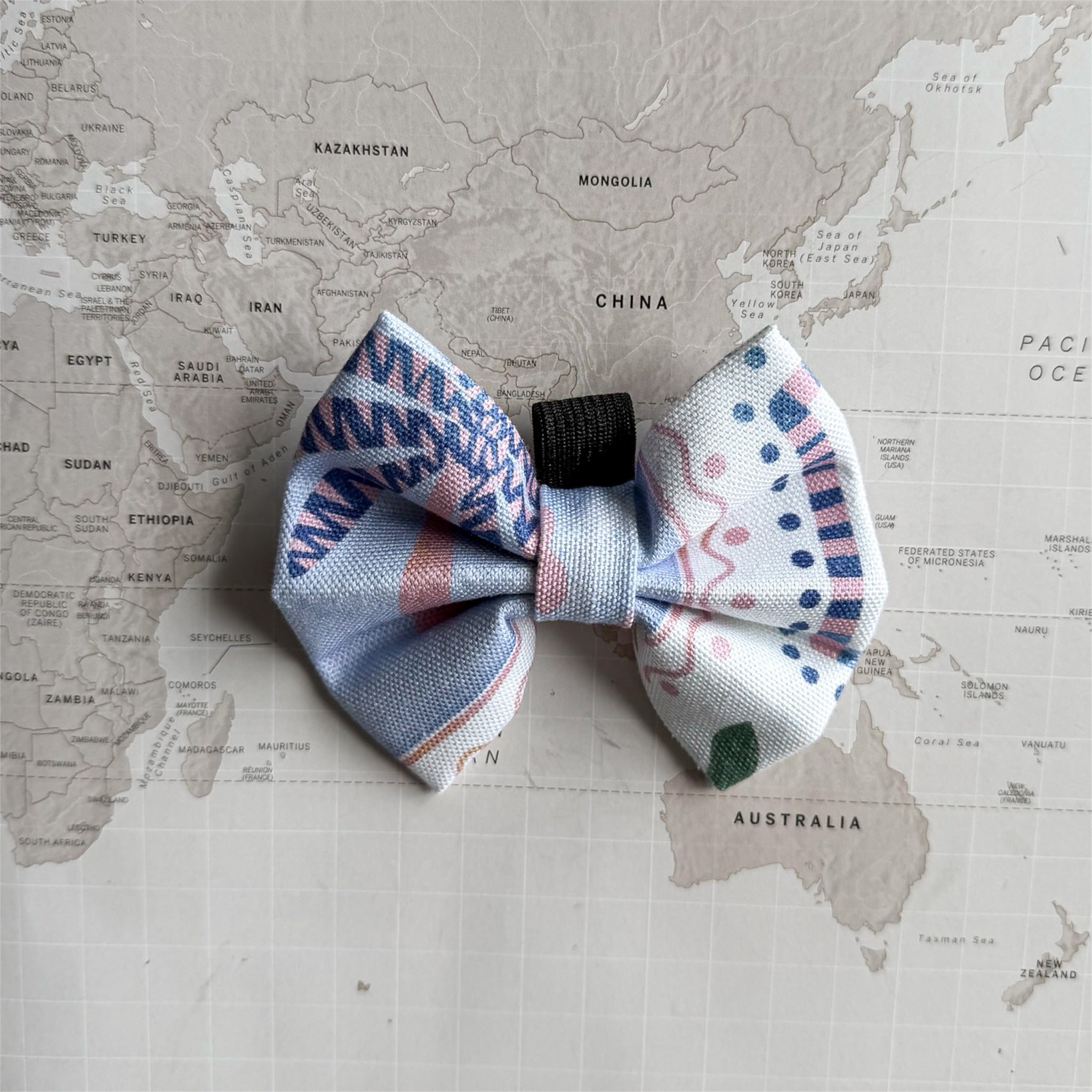 Handmade dog bow with pastel palm tree on a world map background. 