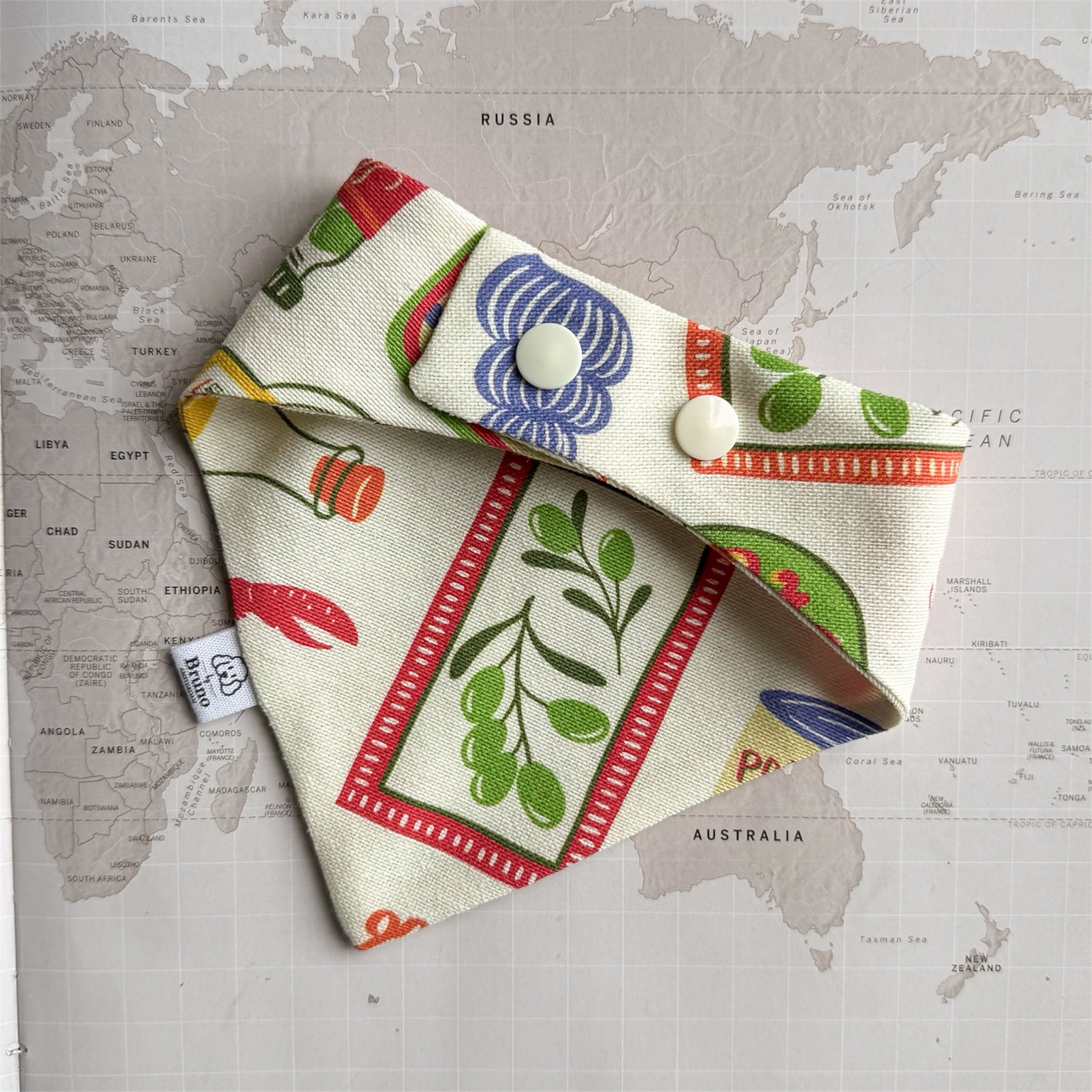 Back side of the Ristorante al mare dog bandana with fish, crab and pasta with plastic beige buttons on a world map background.