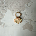 Coastal personalised dog ID tag shaped like a beige seashell on a world map background.