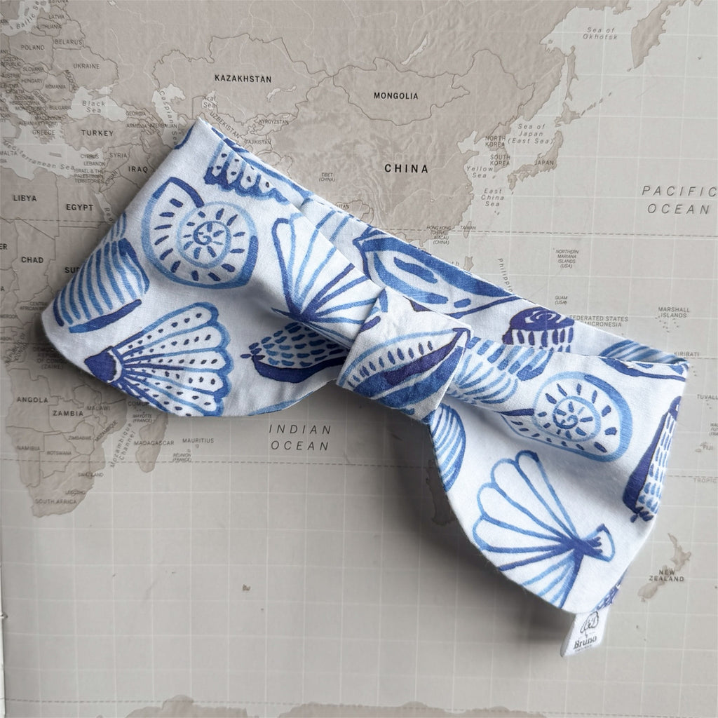 White bow bandana with blue shells on a world map background.