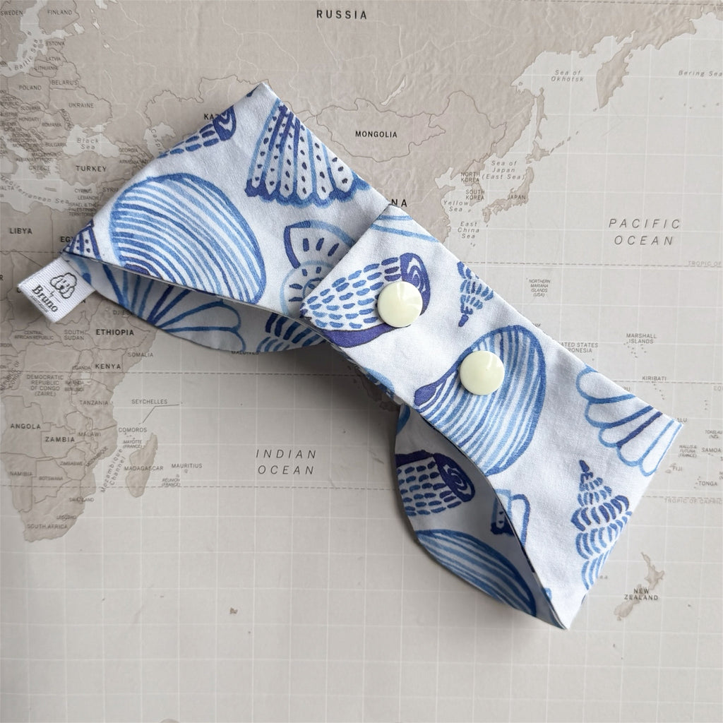 Back side of the white bow bandana with blue shells and plastic buttons on a world map background.