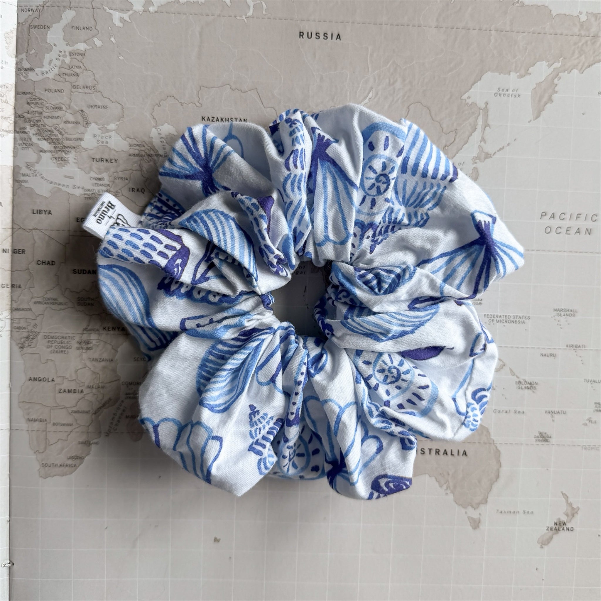 Coastal-inspired scrunchie matching the Seashells dog bandana on a world map background.