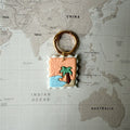 Handmade Summer Postcard dog tag shaped like a stamp with wave, palm tree and sun design on a world map background.