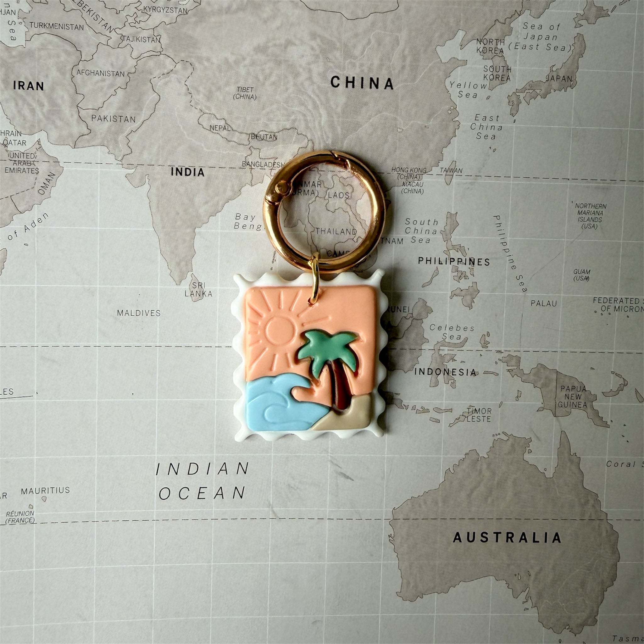 Handmade Summer Postcard dog tag shaped like a stamp with wave, palm tree and sun design on a world map background.