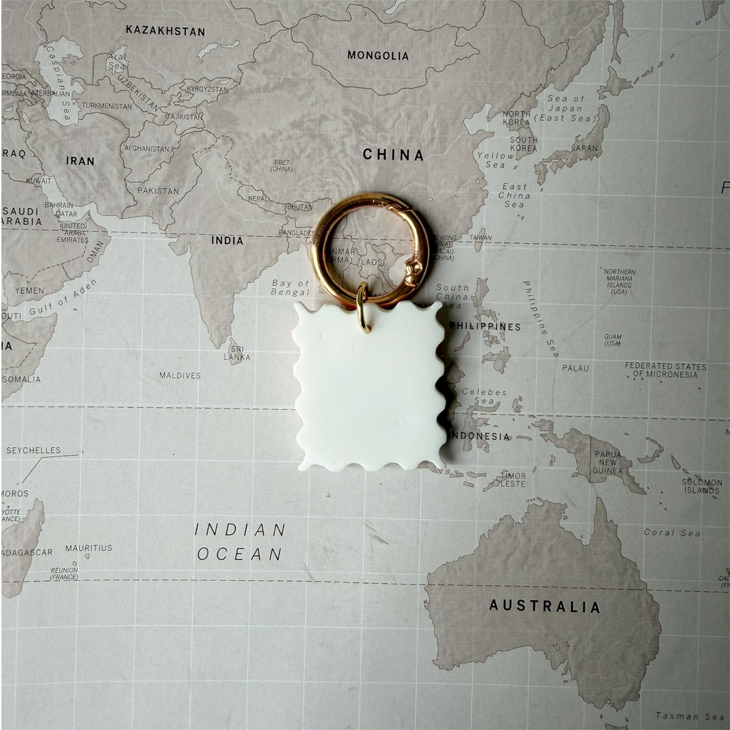 Back side Hof the hndmade Summer Postcard dog tag shaped like a stamp with wave, palm tree and sun design on a world map background.
