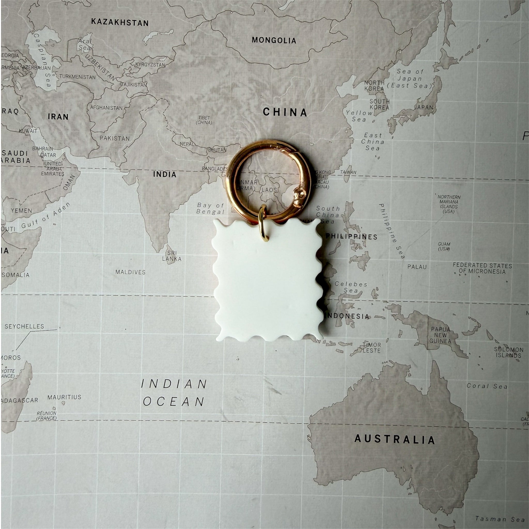 Back side Hof the hndmade Summer Postcard dog tag shaped like a stamp with wave, palm tree and sun design on a world map background.